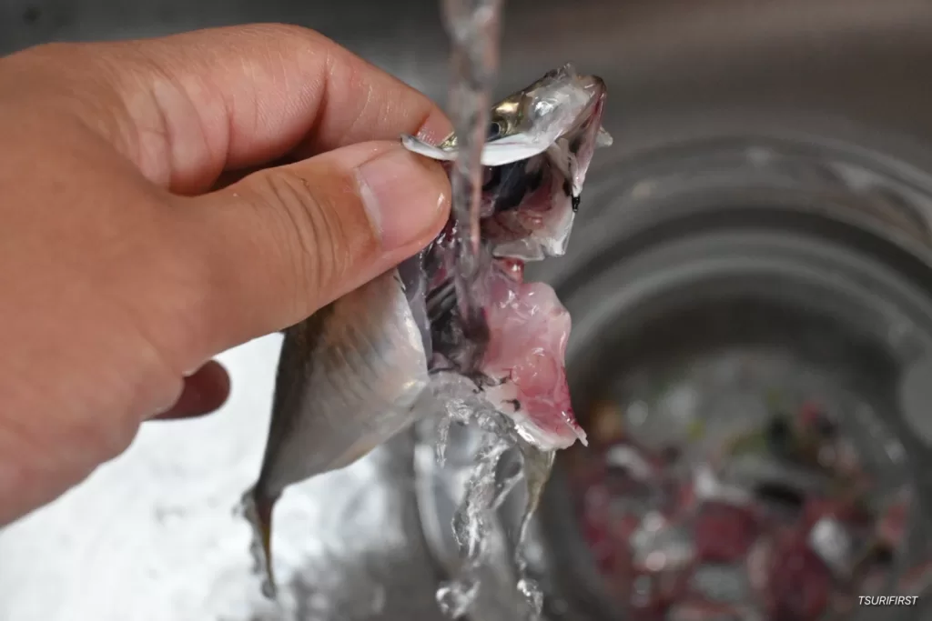 アジの内臓を取り出した後、残った内臓や血を水道水などで洗い流している状態